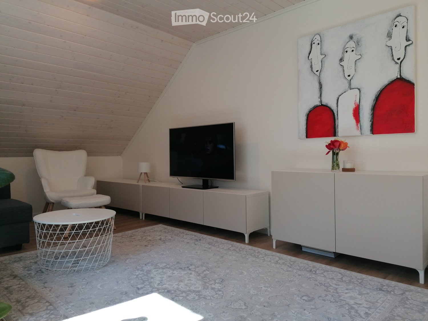 Modern living room with a white sofa, armchair, round coffee table, flat-screen TV on a white cabinet, and a large abstract painting above.