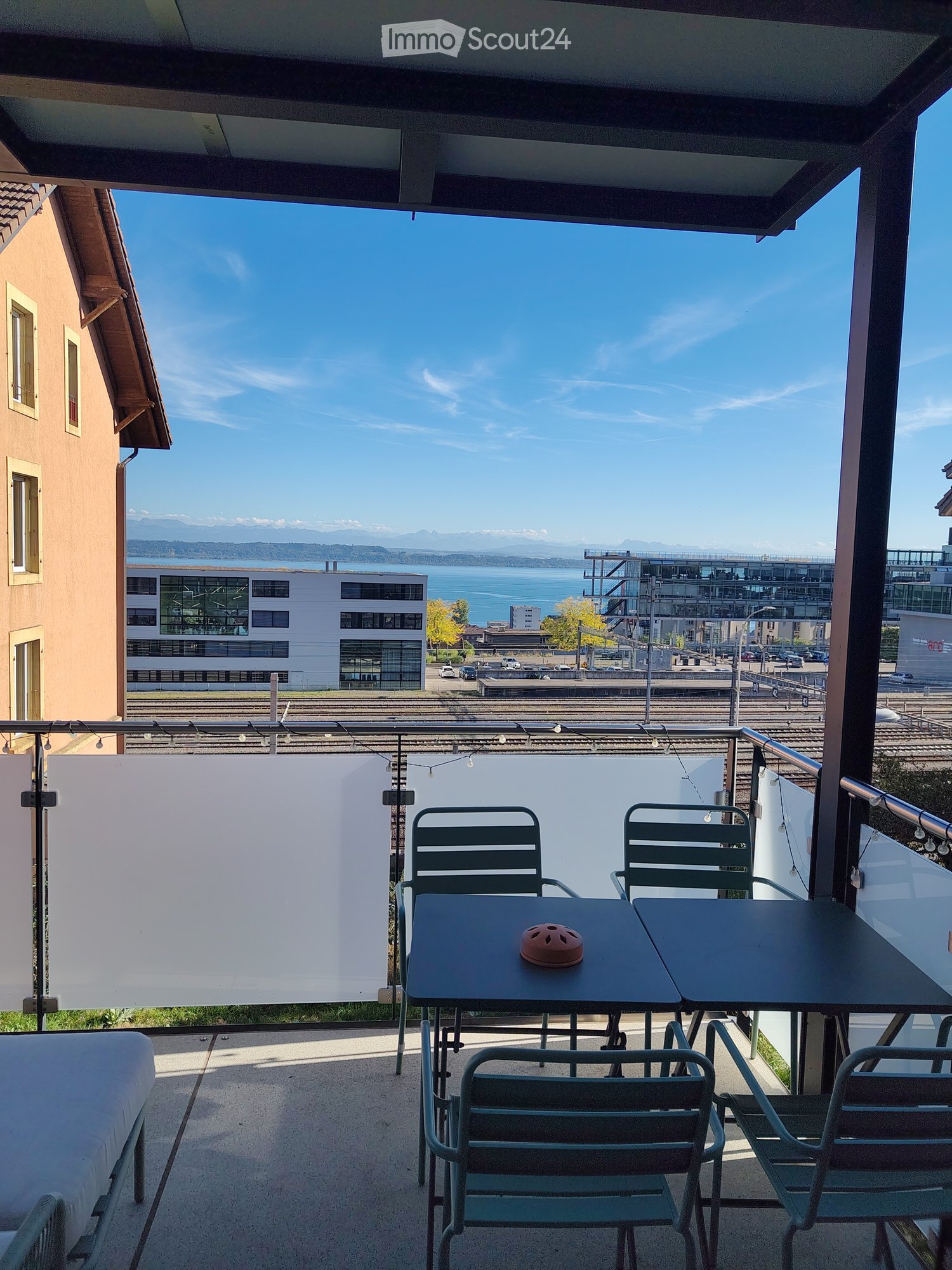 Balcony with outdoor furniture, offering a scenic view of a lake and distant mountains.