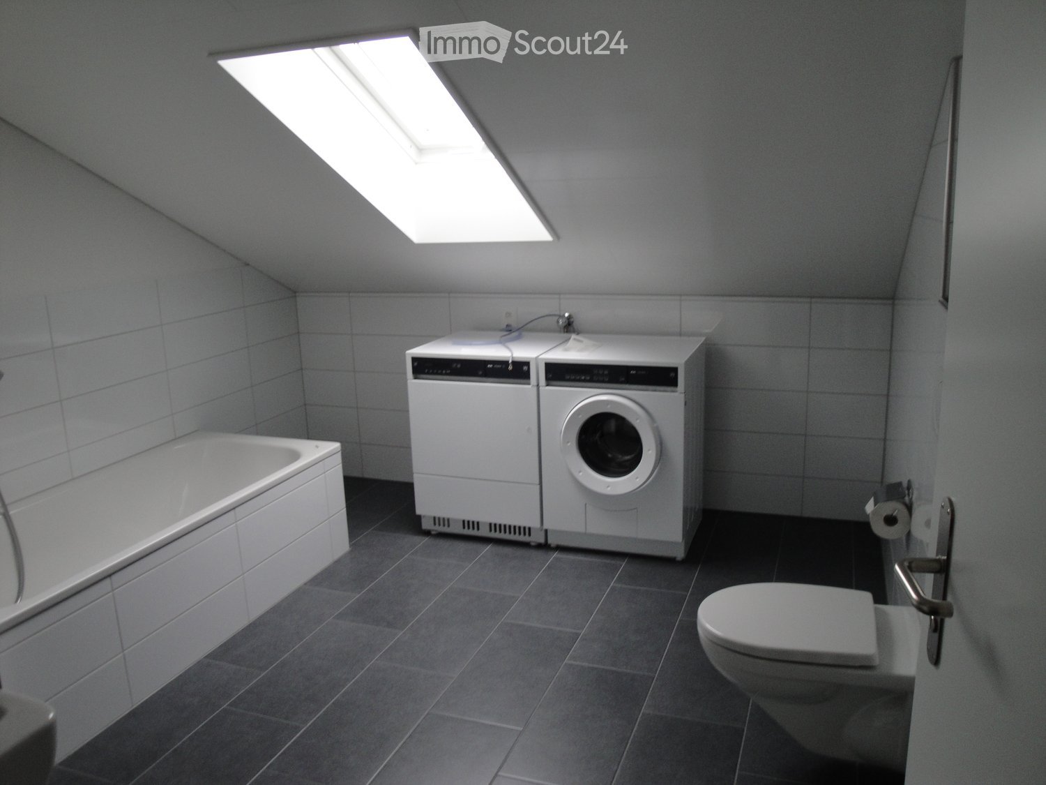 Modern bathroom with a bathtub, toilet, washing machine, and a skylight window providing natural light.