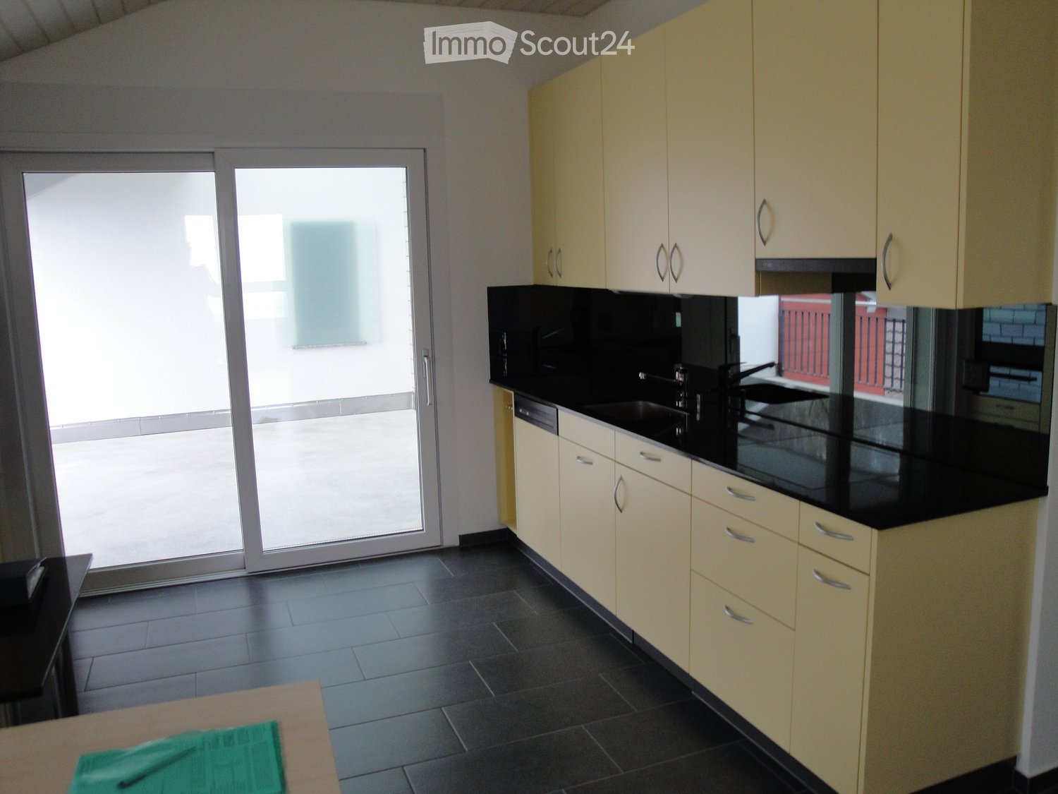 Modern kitchen with light-colored cabinets, black countertops, and a large sliding glass door leading to a balcony.