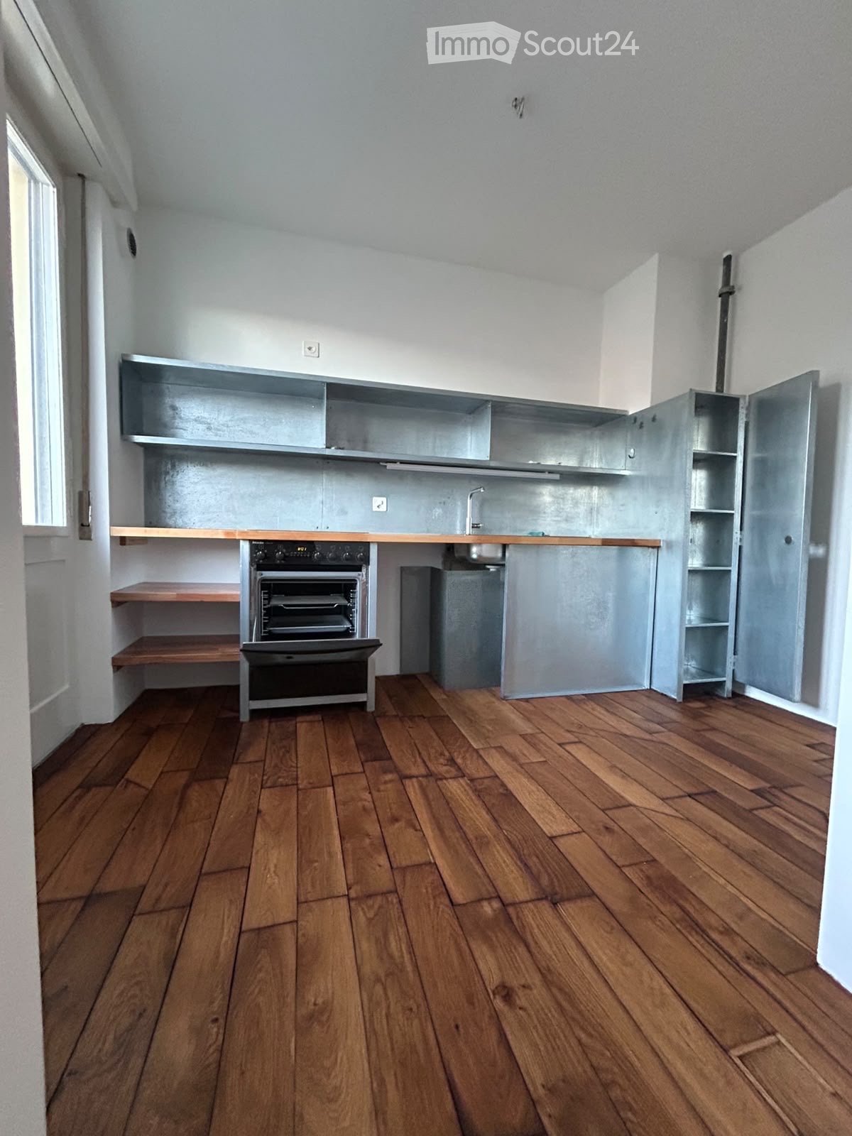 Modern kitchen with wooden flooring, stainless steel appliances, and open shelving.