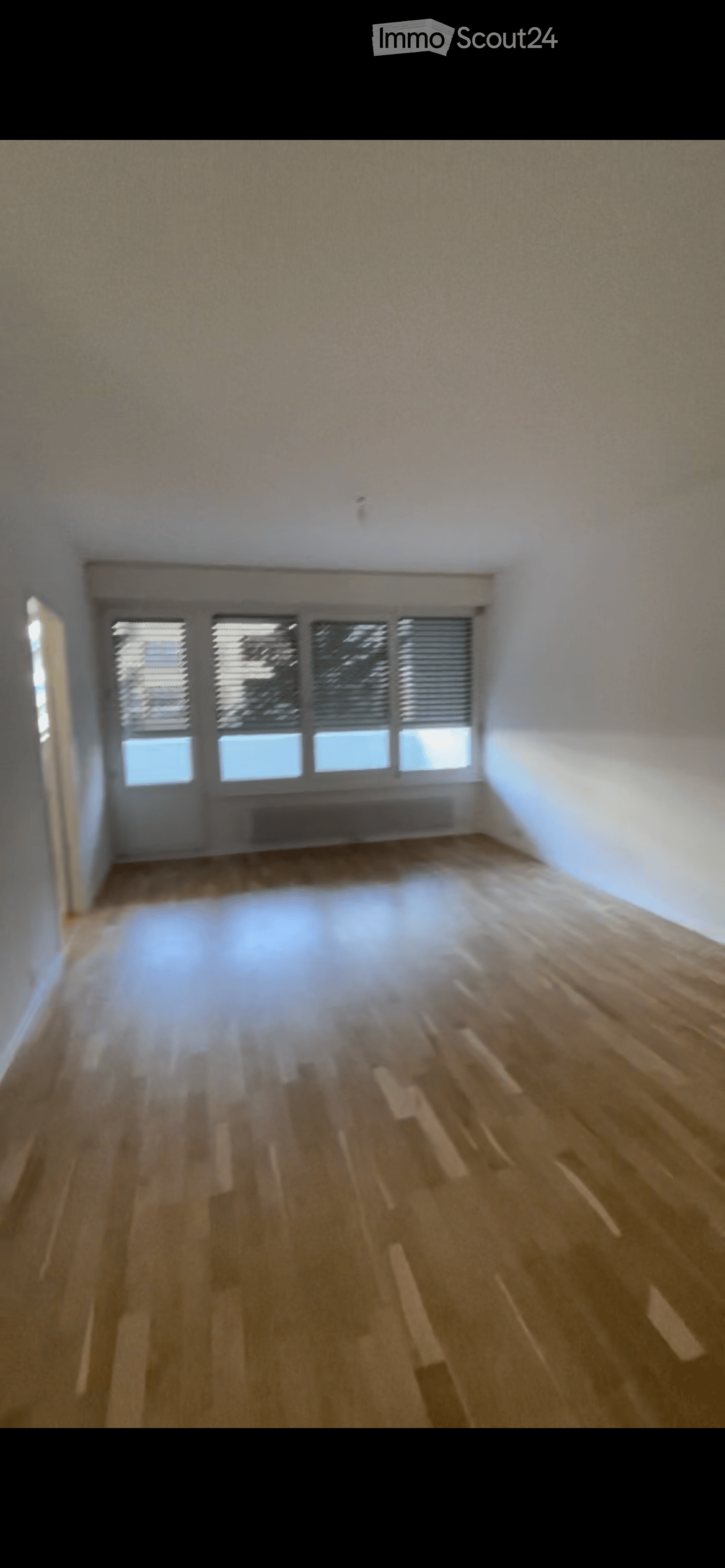 Empty room with wooden flooring, white walls, and large windows with blinds. No furniture or equipment present.