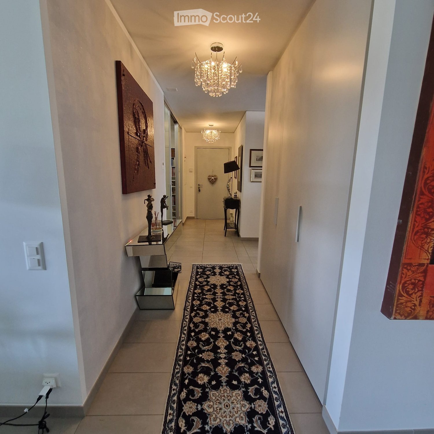 Elegant hallway with a patterned runner, modern lighting fixtures, and decorative wall art. Features a small console table with a mirror and a small side table with a lamp.