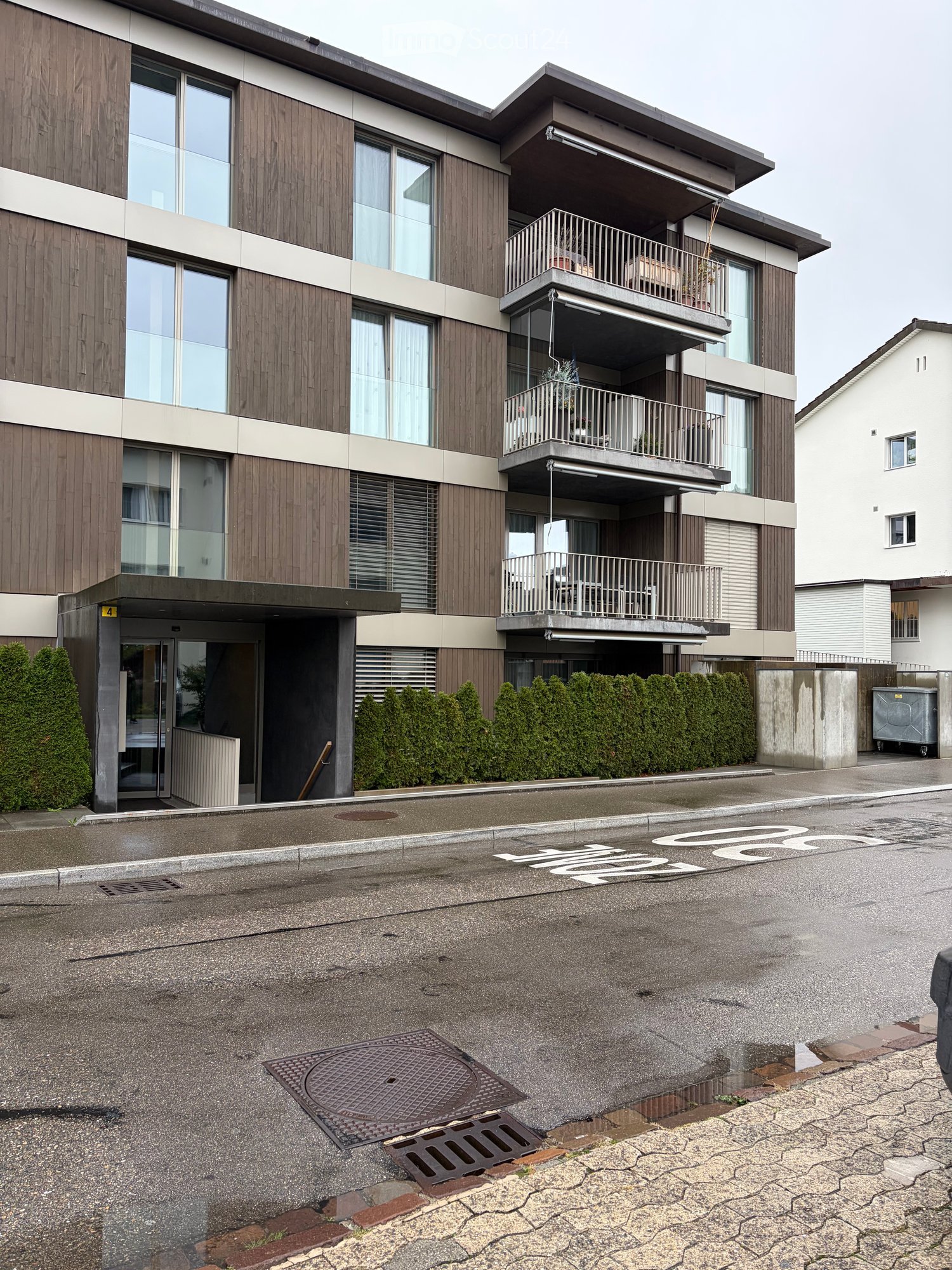 Modern multi-story building with wooden facade, large windows, and balconies with railings.