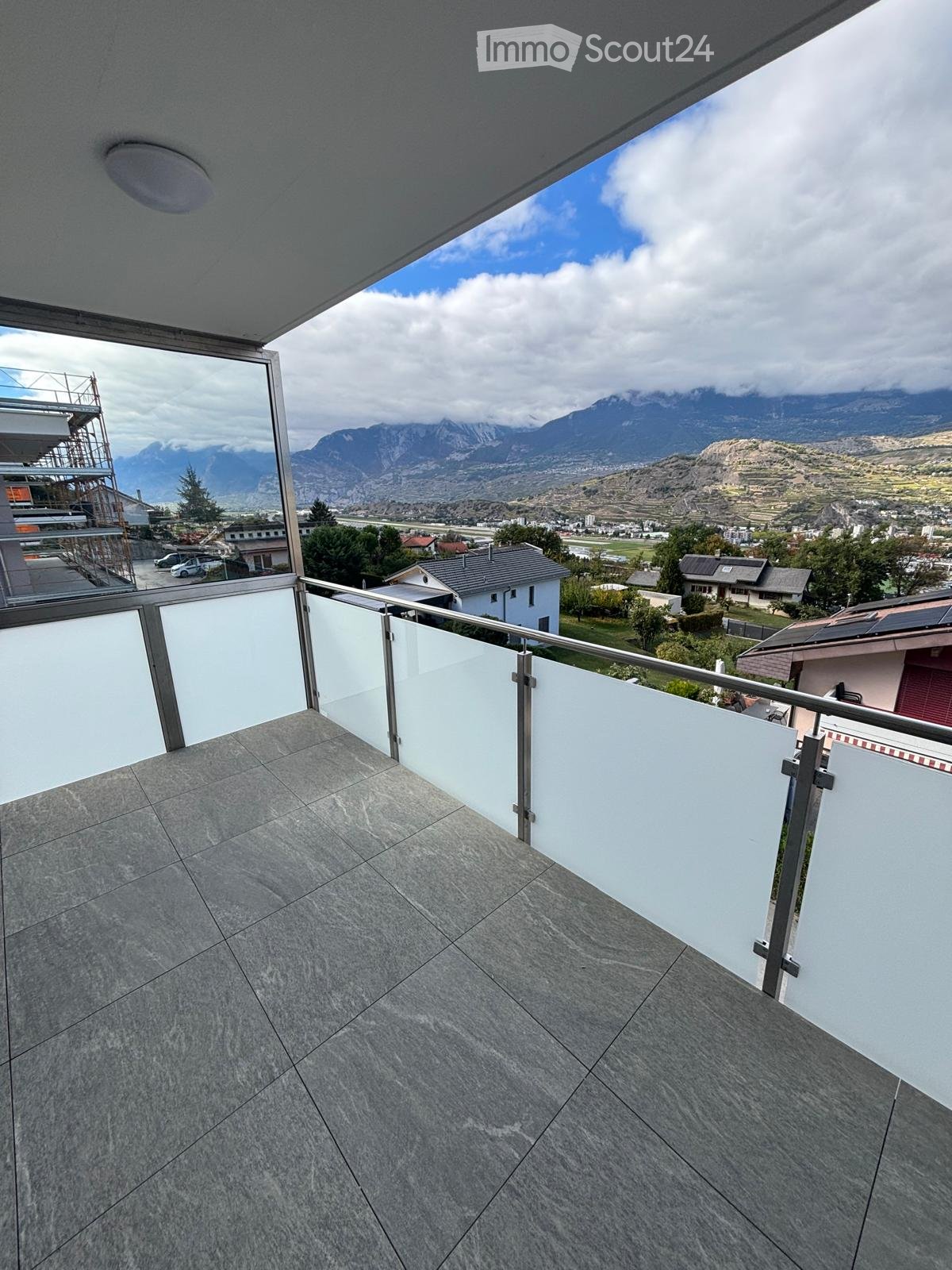 Balcony with modern glass railing, tiled floor, and scenic mountain view.
