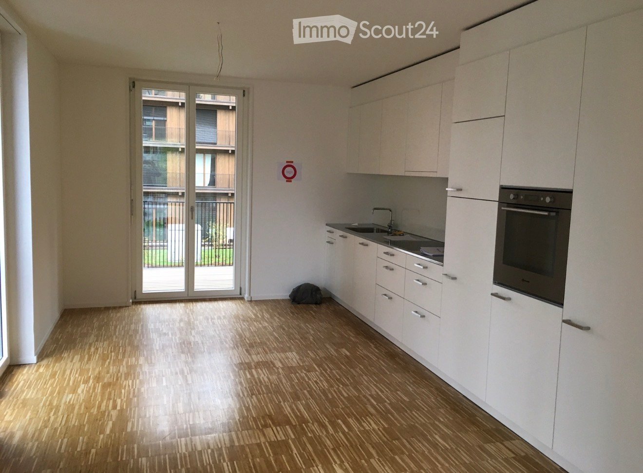 Modern kitchen with white cabinets, wooden flooring, and a large sliding glass door leading to a balcony.