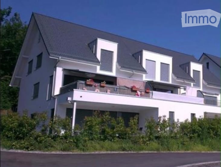 Modern two-story house with white exterior, grey roof, and a large balcony on the upper floor.