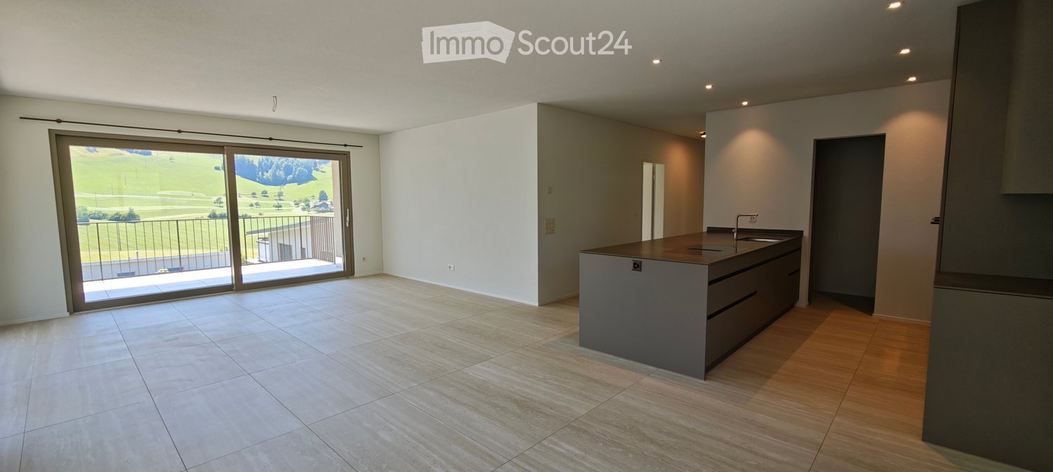Modern kitchen with a central island, large sliding glass doors leading to a balcony with a scenic view, and a mix of tile and wood flooring.