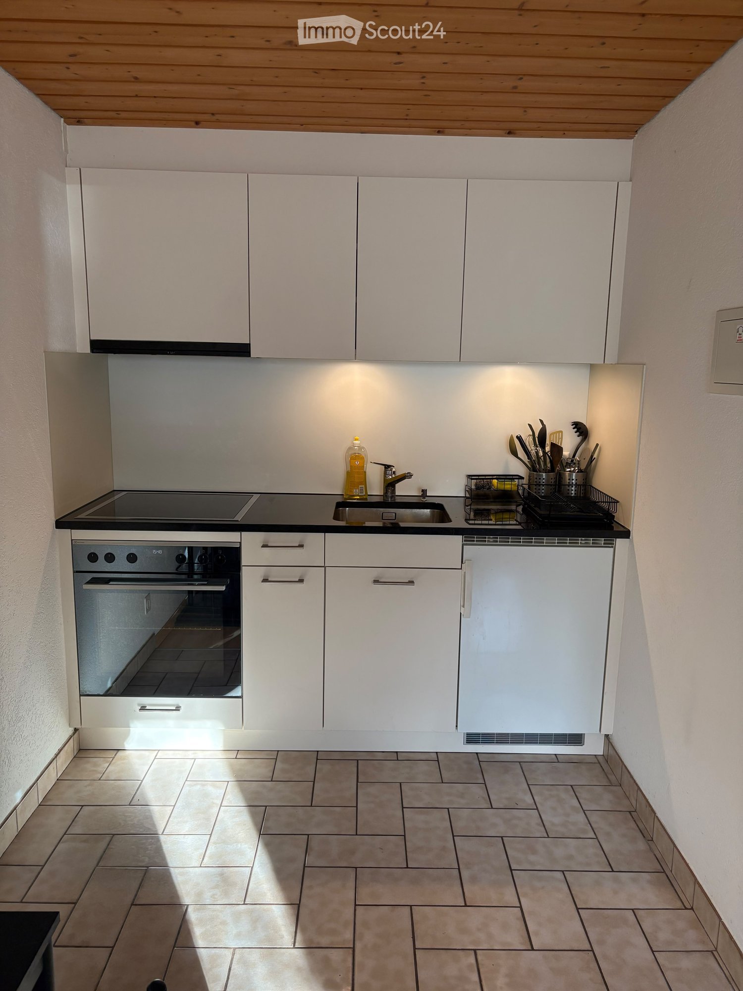 Modern kitchen with white cabinets, black countertop, induction cooktop, oven, sink, and various kitchen utensils on the counter.