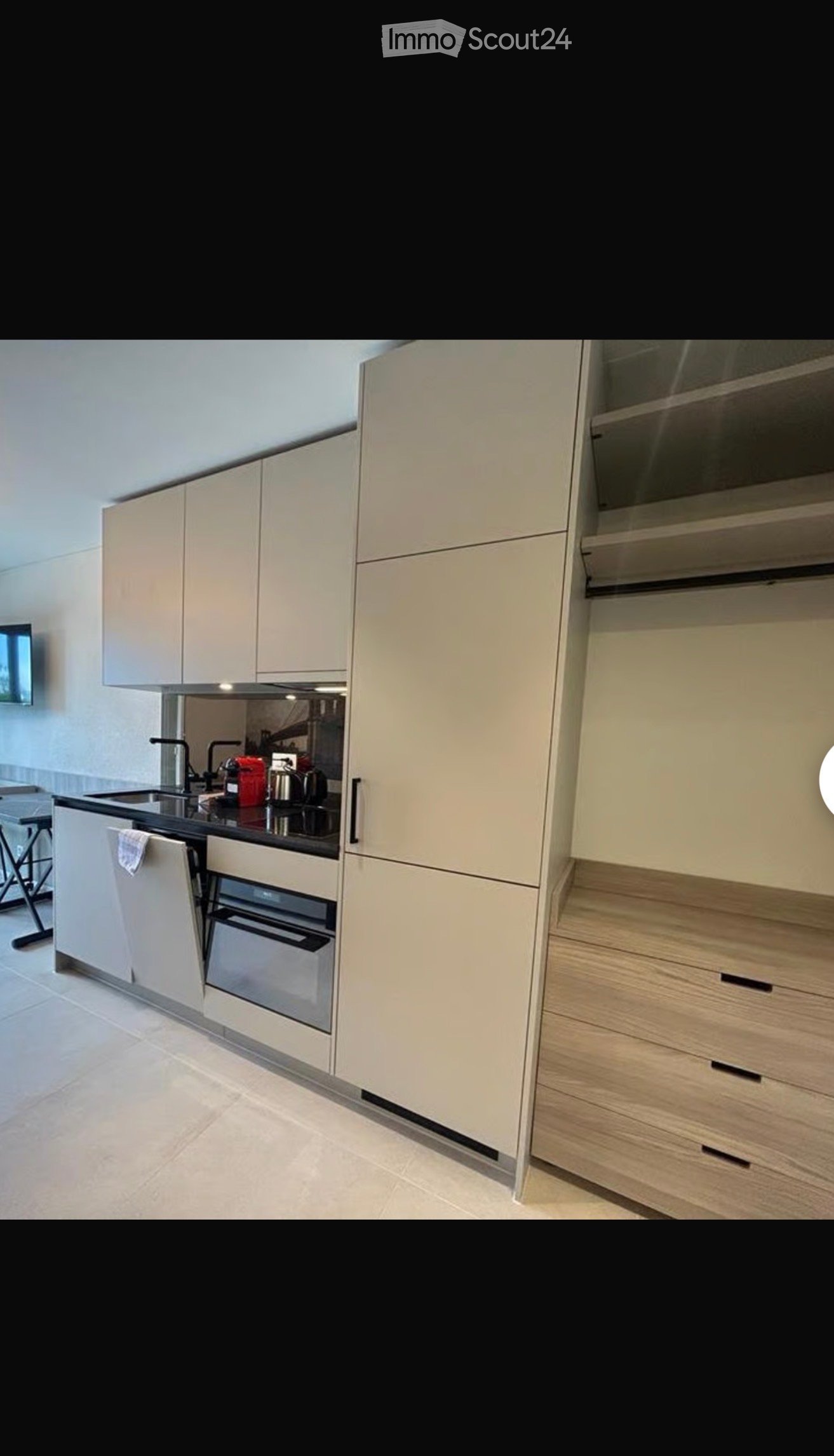 Modern kitchen with light-colored cabinets, a black countertop, and stainless steel appliances including a sink, oven, and faucet.