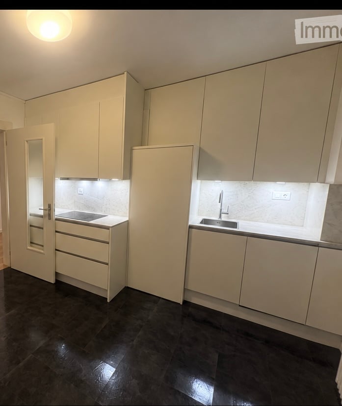 Modern kitchen with light-colored cabinets, dark wooden flooring, and built-in appliances including a stove and sink.