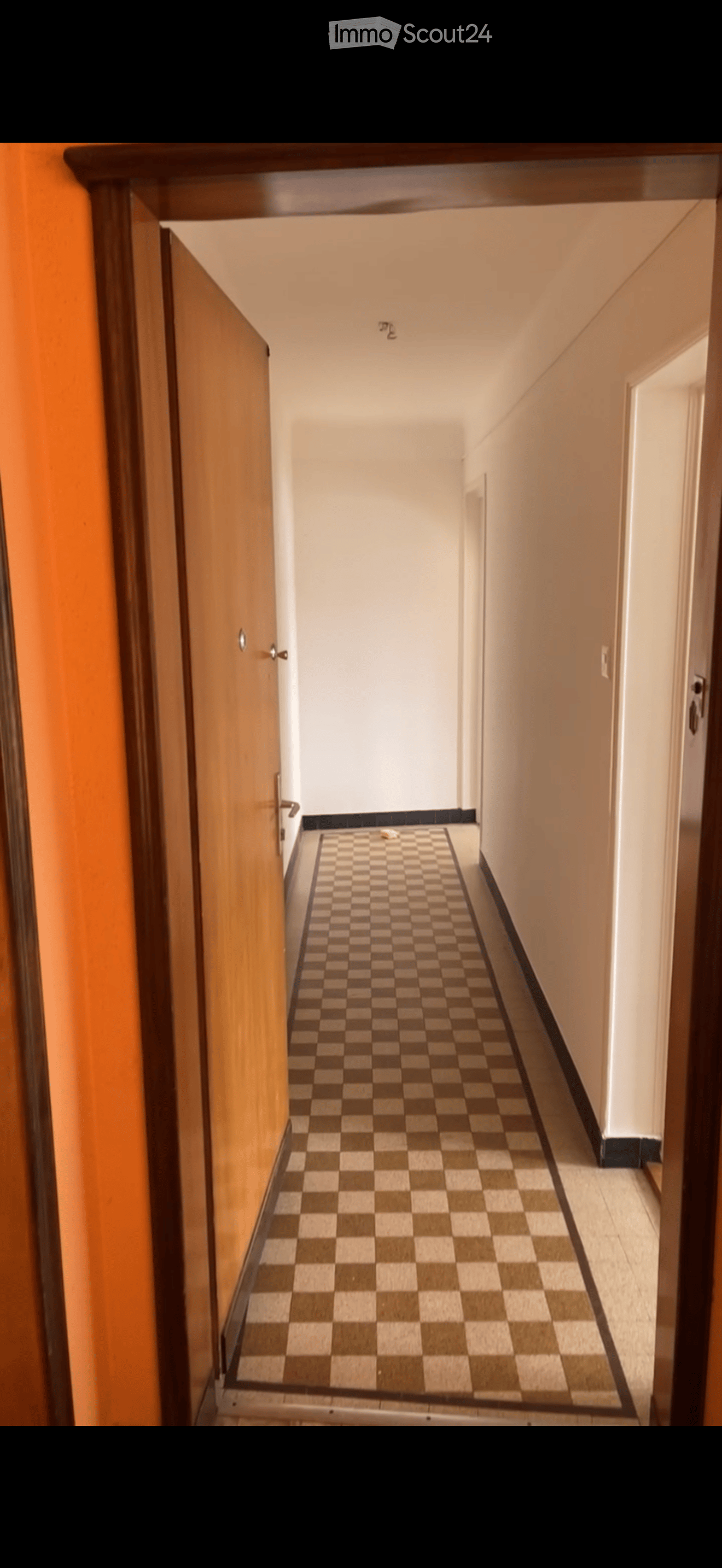 A narrow hallway with a checkered floor, light-colored walls, and wooden doors on both sides.