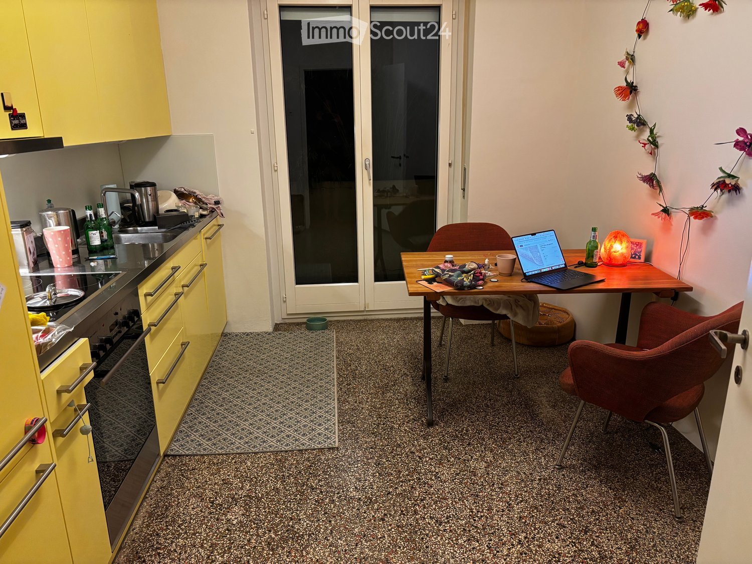 A compact kitchen and workspace area with yellow cabinets, a stove, sink, and a small table with a laptop and chairs.