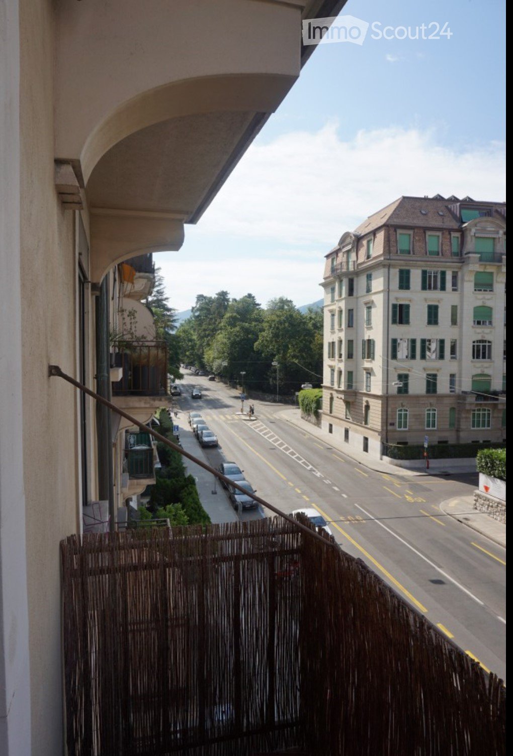Balcony overlooking a street with cars, buildings, and greenery in the background.