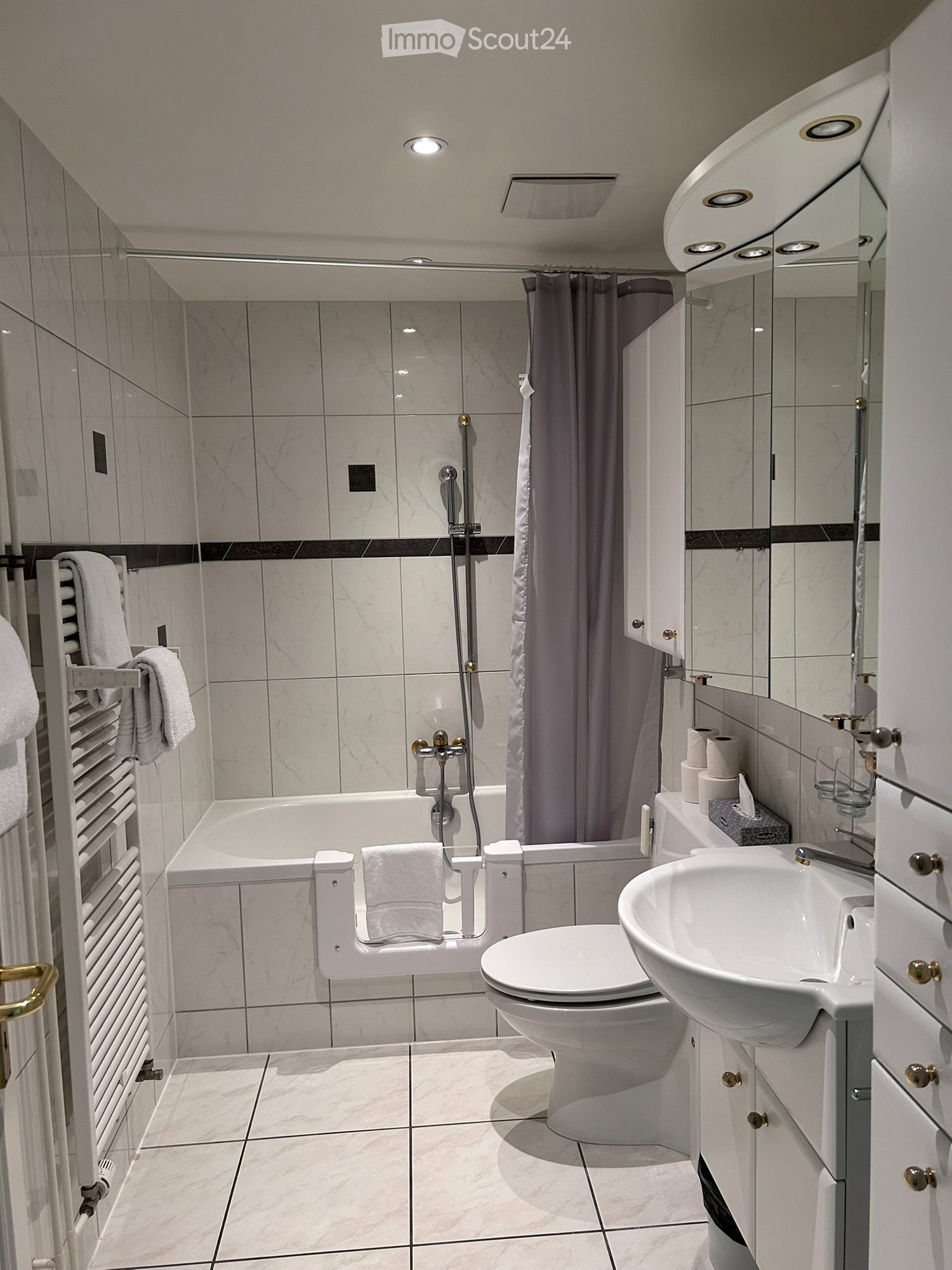 Modern bathroom with marble tiles, bathtub, toilet, sink, mirror, and towel rack with towels.
