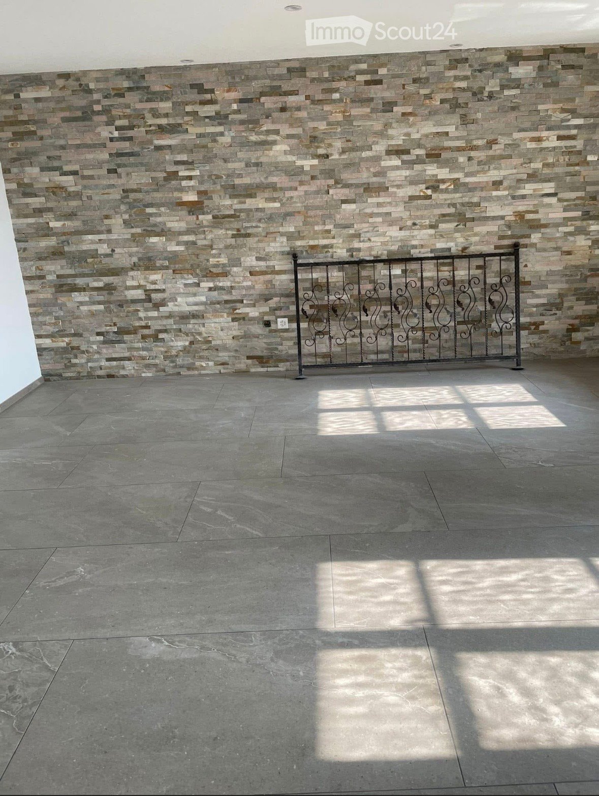 Empty room with a tiled wall and a decorative metal gate, featuring a concrete floor and natural light from an unseen source.