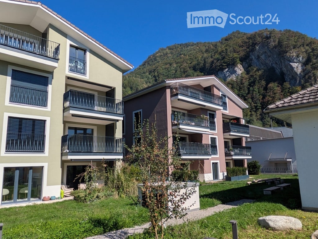 Modern multi-story residential building with balconies overlooking a green lawn and mountain view.
