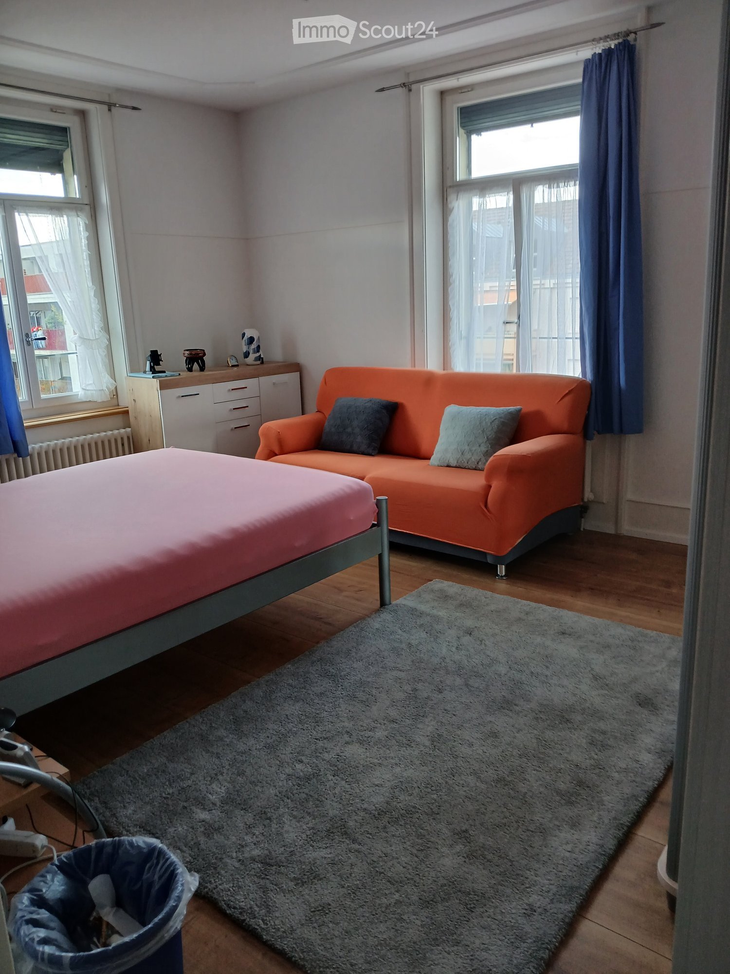 A cozy bedroom with a bed, orange sofa, and a grey rug on wooden flooring.