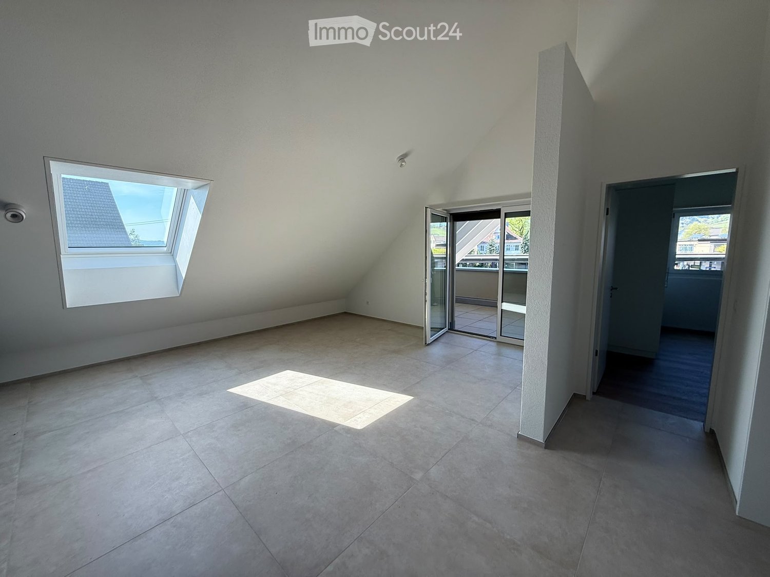 Empty attic room with tiled floor, skylight window, and sliding glass door leading to a balcony.
