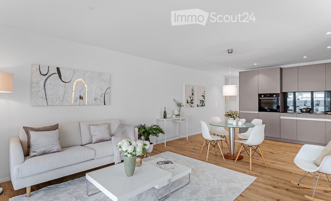 Modern, open-concept living and dining area with a white sofa, coffee table, dining table with chairs, kitchen area with cabinets and appliances, and decorative artwork on the walls.