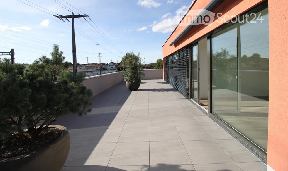 Balcony with tiled floor, glass sliding doors, potted plants, and a view of the surrounding area.
