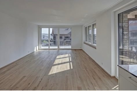 Bright, empty room with wooden flooring, large windows, and sliding glass doors leading to an outdoor area.