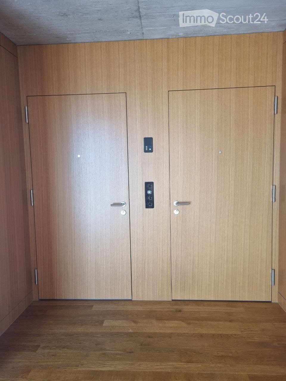 Empty hallway with wooden doors and a polished wooden floor, featuring modern door handles and a small control panel.