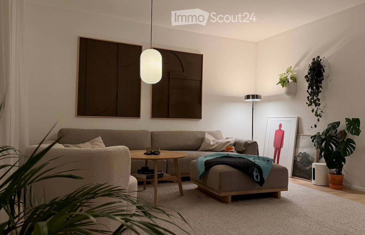 Modern living room with a grey sectional sofa, wooden coffee table, ottoman, floor lamp, and decorative art pieces.
