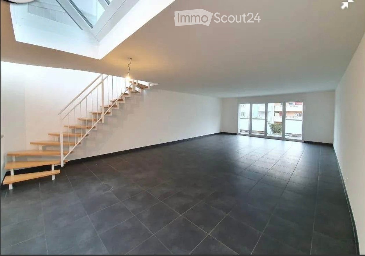 Empty room with dark tiled floor, white walls, and a staircase leading to an upper level. Large window and skylight provide natural light.