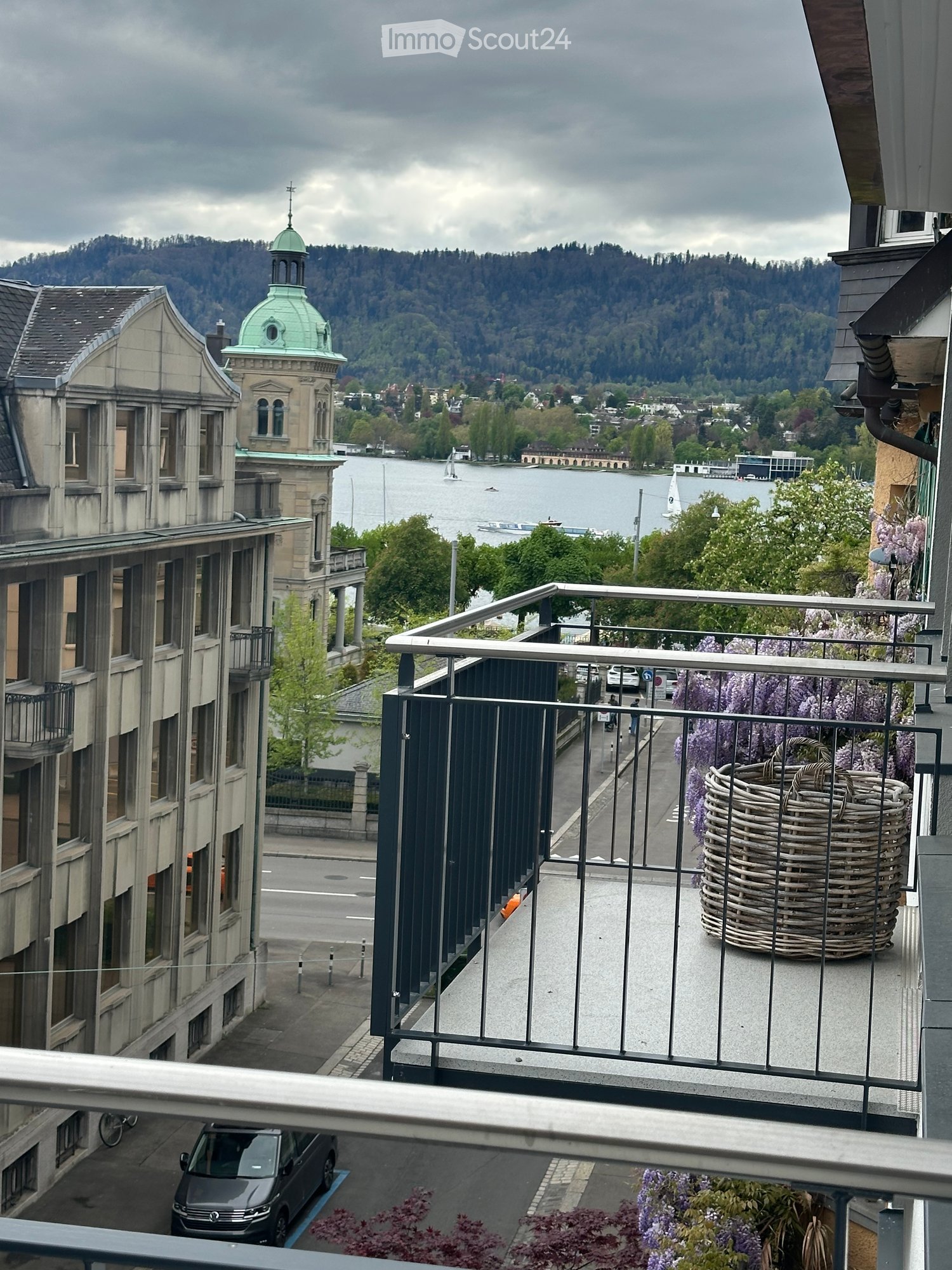 Balcony with metal railing, overlooking a scenic lake and cityscape with a prominent church dome in the background.