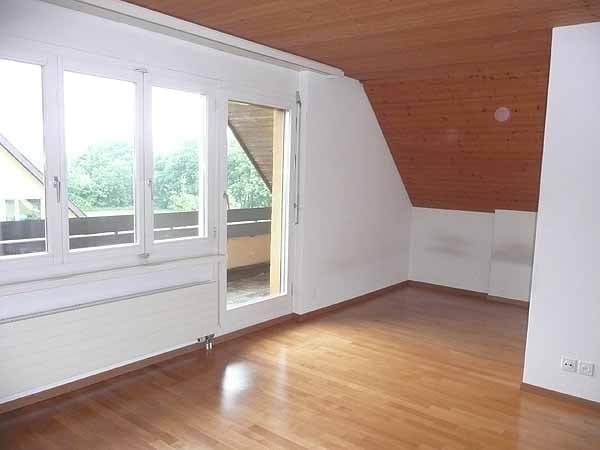 Empty attic room with wooden floor, white walls, large windows, and a sliding glass door leading to a balcony.