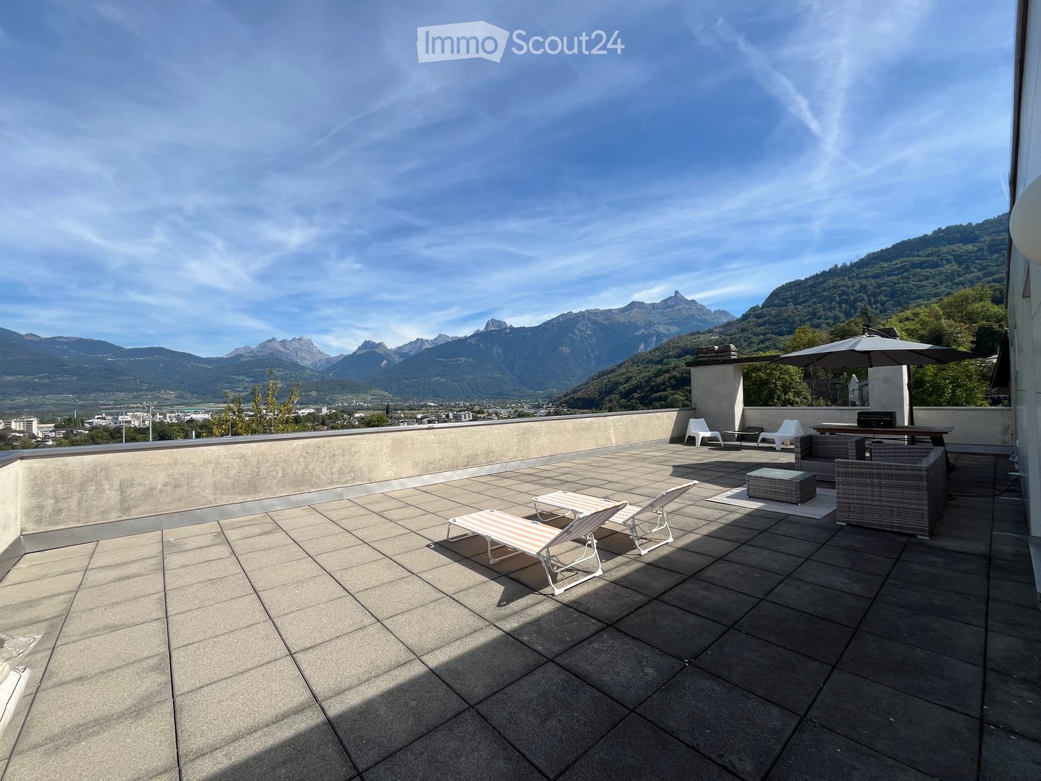 Roof terrace with tiled floor, lounge chairs, small table, umbrella, and scenic mountain view.