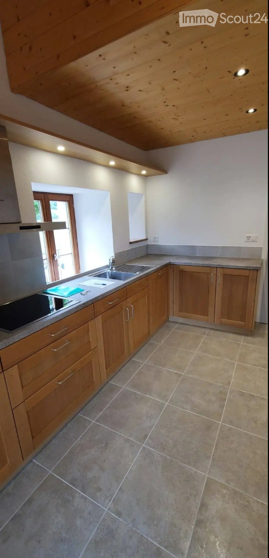 Modern kitchen with wooden cabinets, stainless steel sink, and tiled floor.