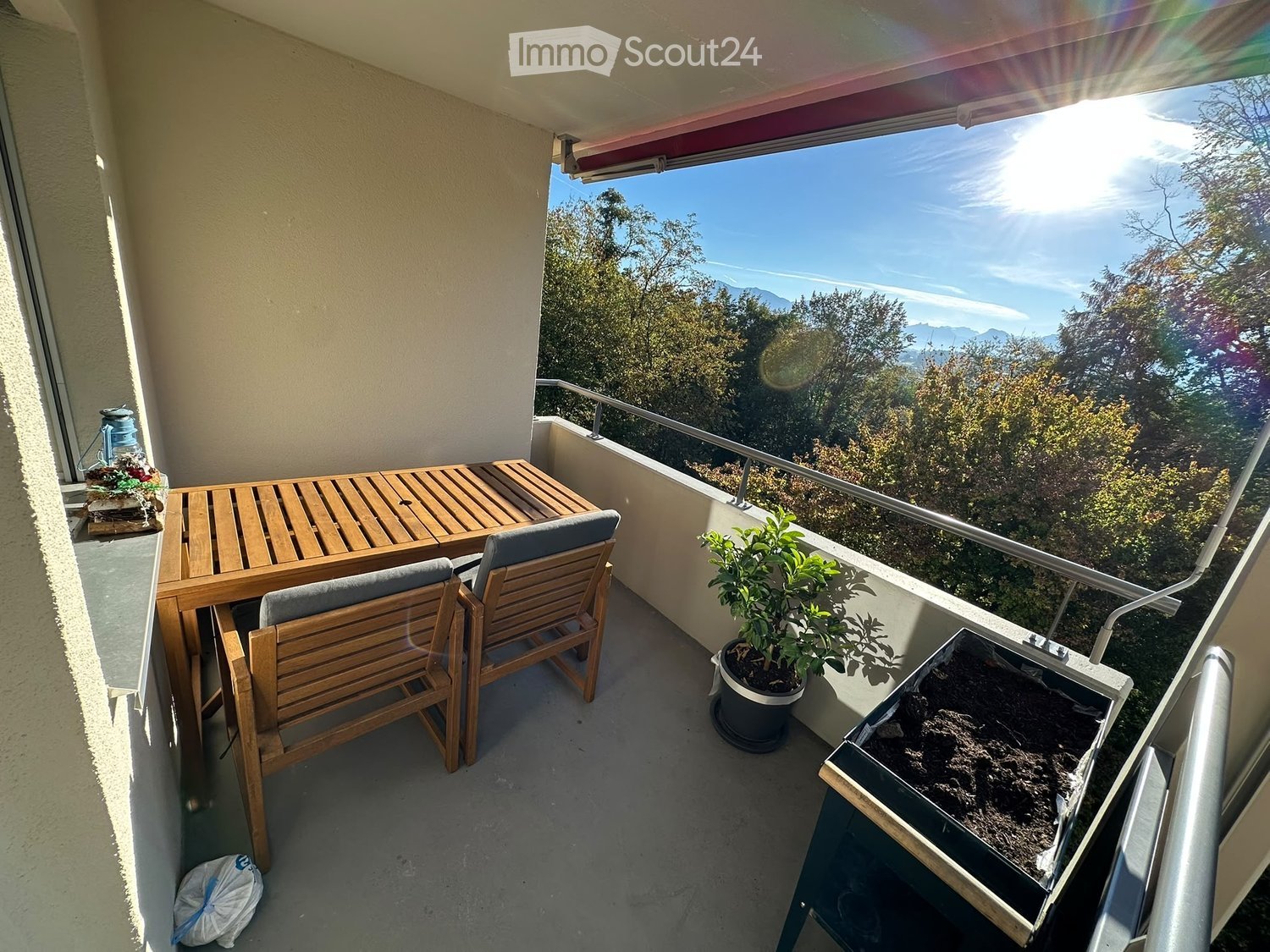 Balcony with wooden table and chairs, potted plant, scenic mountain view.