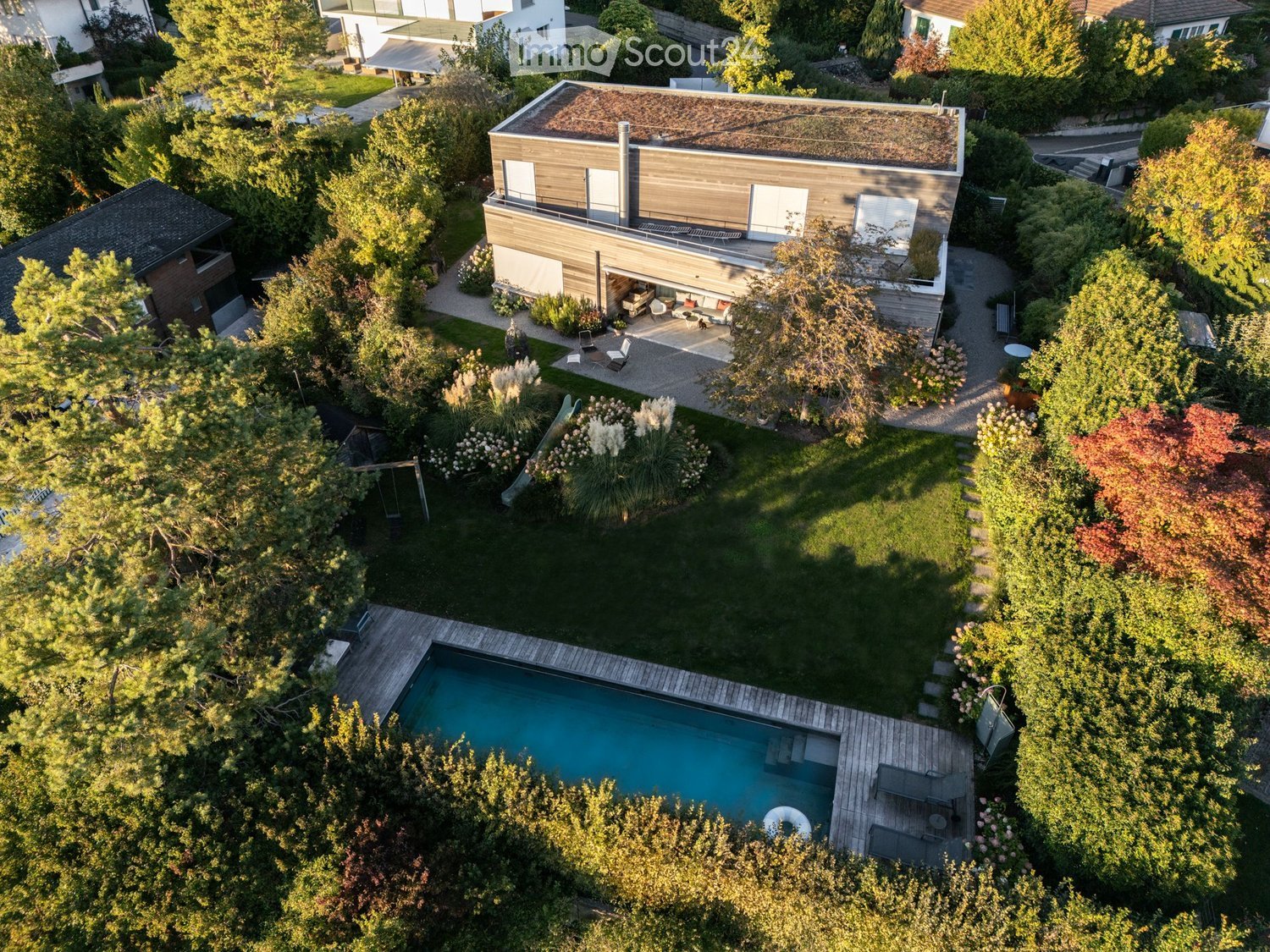 Aerial view of a modern house with a swimming pool, surrounded by a well-maintained garden and trees.