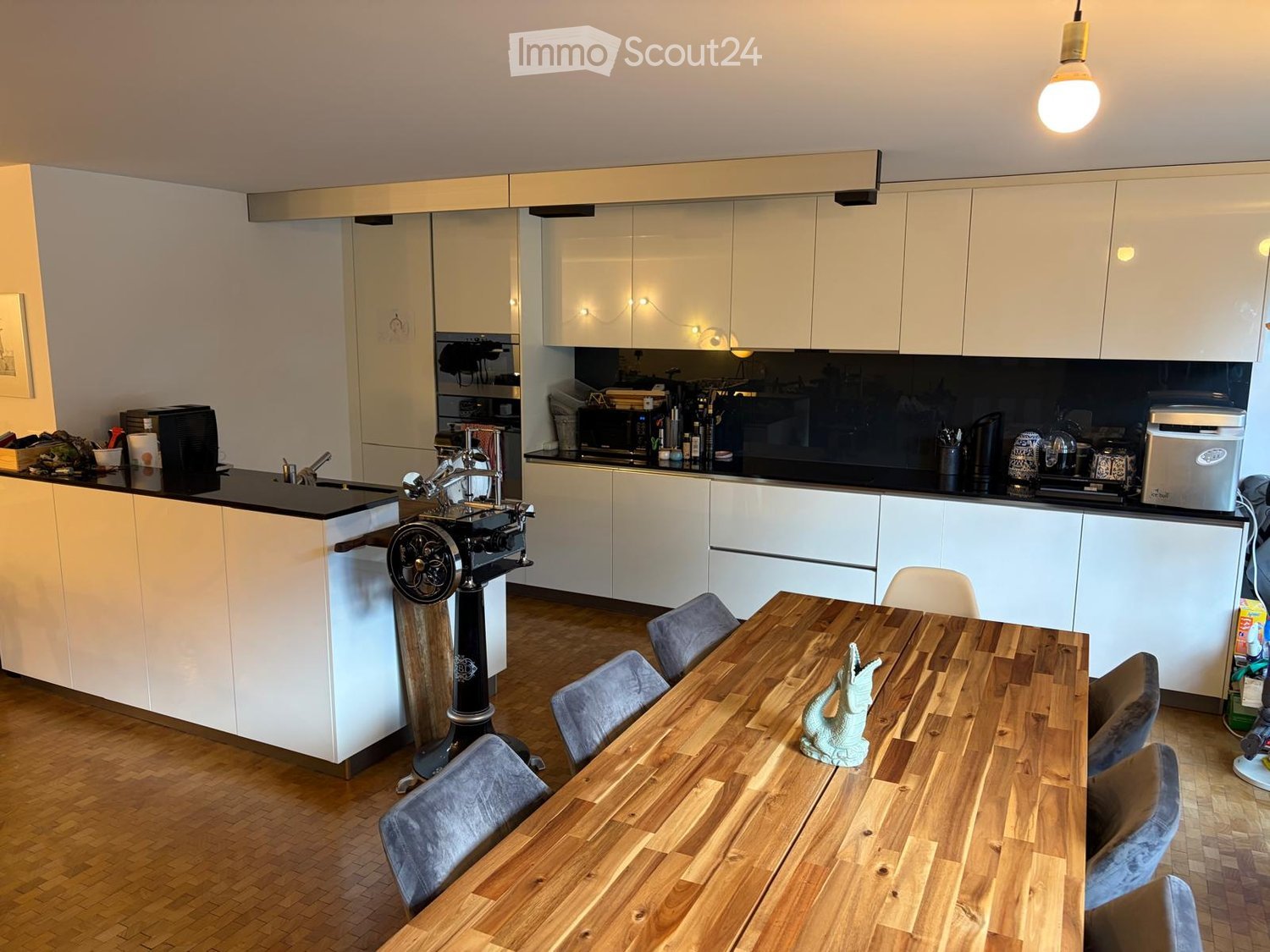 Modern kitchen with white cabinets, wooden dining table, and various appliances.
