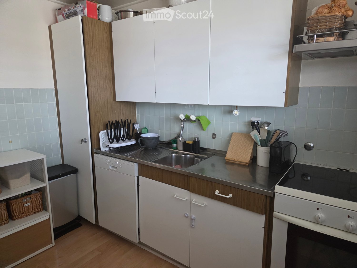 Modern kitchen with white cabinets, wooden accents, stainless steel appliances, and various kitchen utensils on the counter.