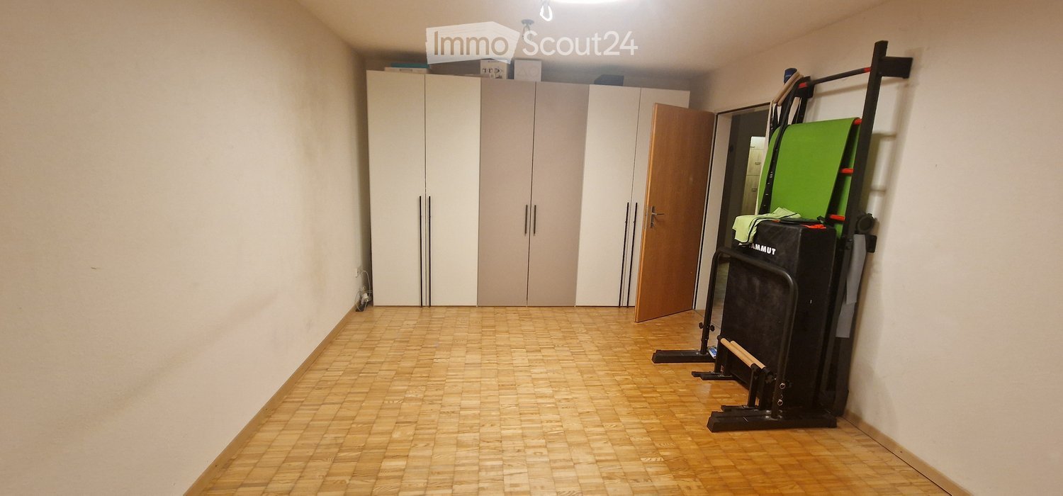 Empty room with wooden flooring, white walls, built-in wardrobes, and a partially open door. A piece of exercise equipment is visible in the corner.