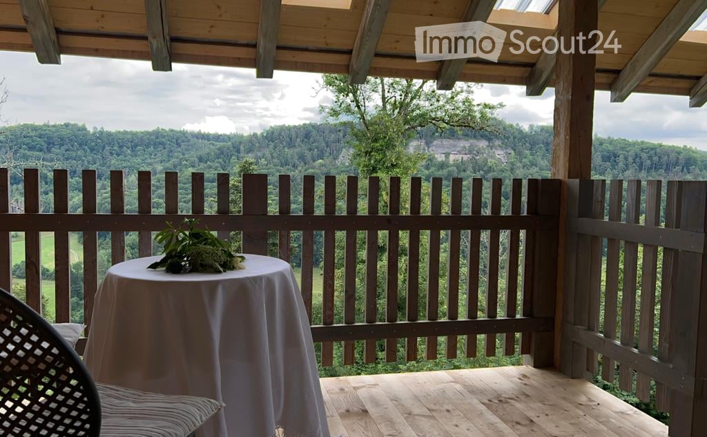 Wooden balcony with a table, chair, and scenic mountain view.