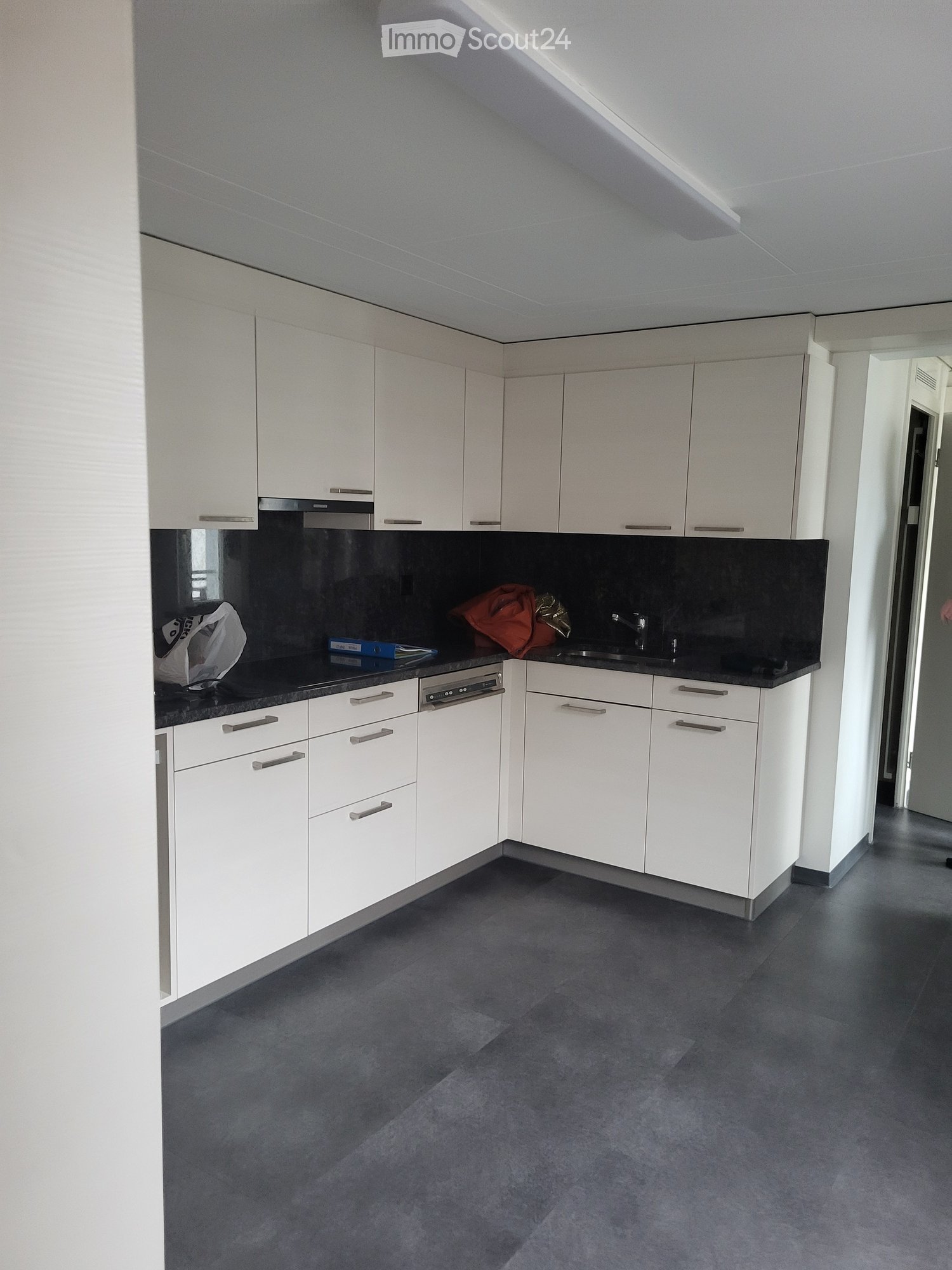Modern kitchen with white cabinets, black countertops, and a dishwasher. The floor is dark grey, and the space is well-lit with a sleek design.