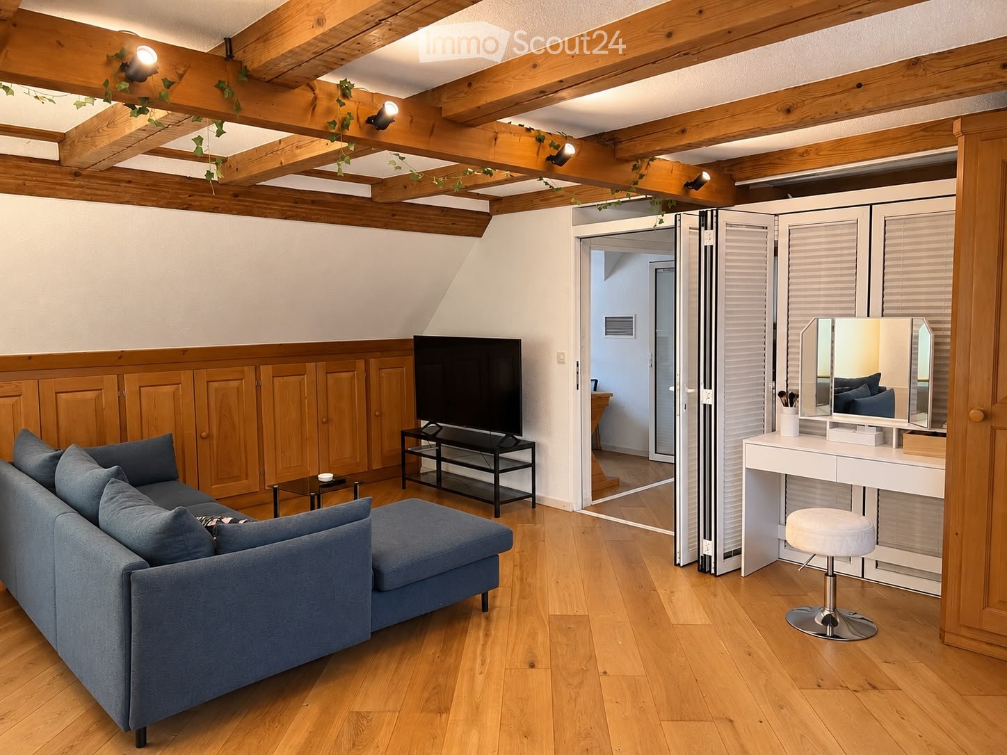 A modern living room with wooden beams, a grey sofa, coffee table, vanity with mirror, and TV stand.