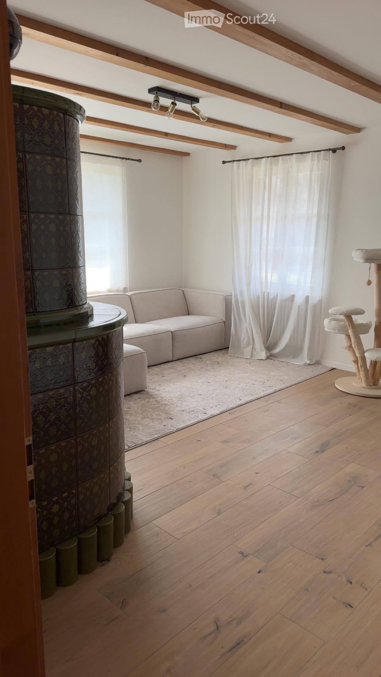 Bright living room with wooden floors, exposed wooden beams, a modern sofa, a cat tree, and a round table with a decorative column.