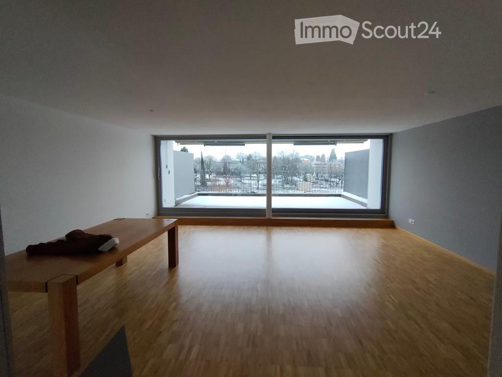 Empty room with wooden flooring, large window, and a small wooden table with a jacket on it.