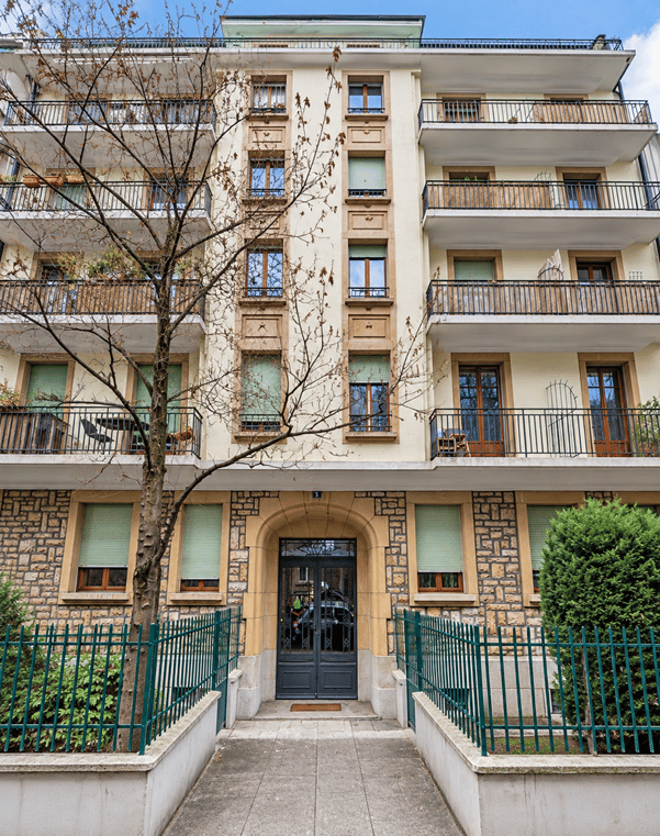 Multi-story residential building with balconies, stone facade, and green metal fence.
