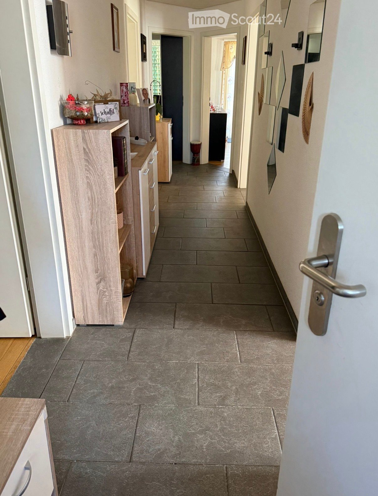 A clean, tiled hallway with light-colored walls, wooden cabinetry on the left, and several doors leading to other rooms.