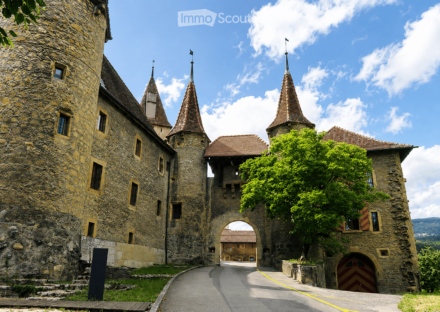 Stone castle with multiple towers, arched gateway, and a clear blue sky background.