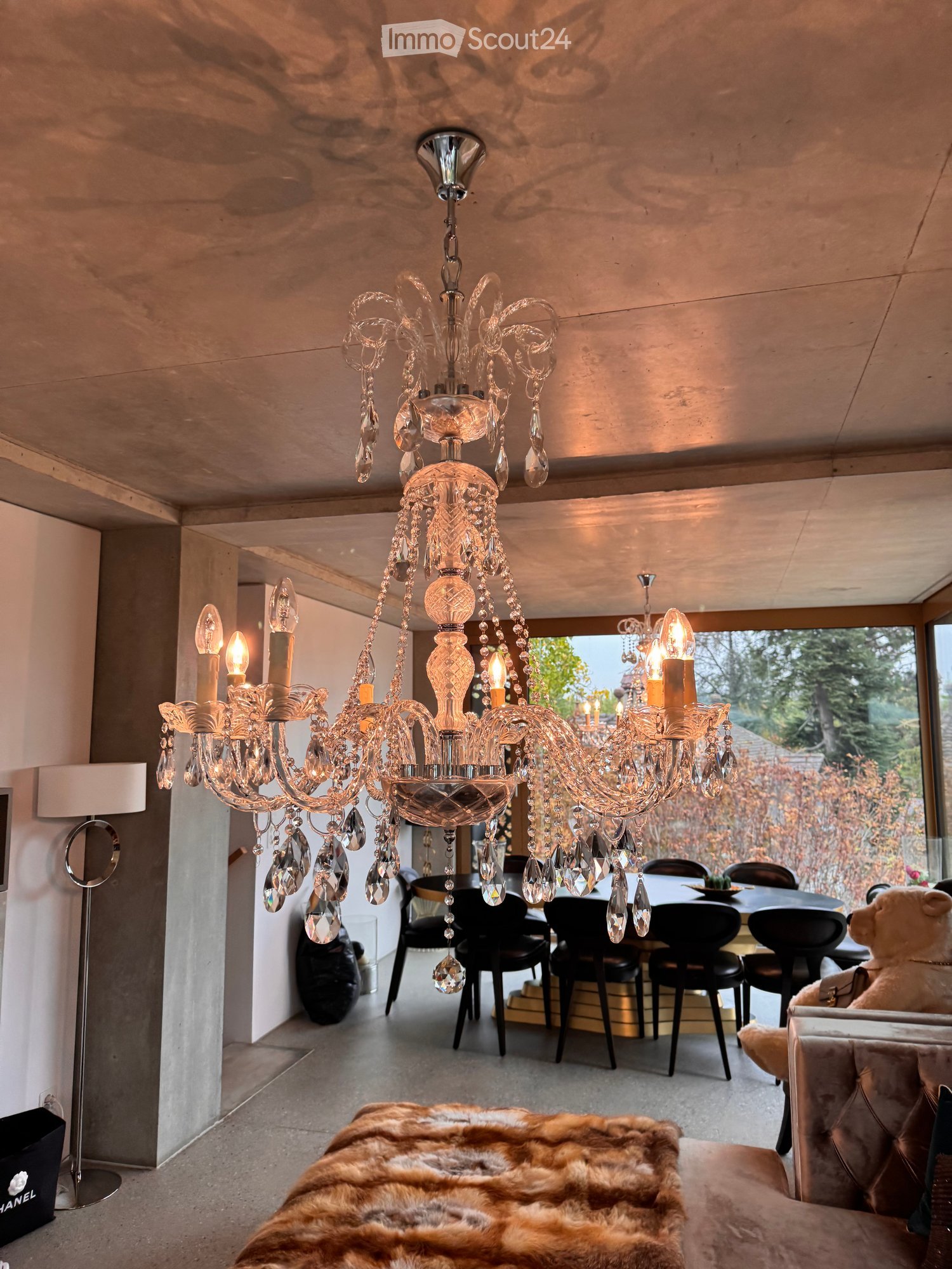 Modern living and dining area with a large chandelier, sofa, dining table, chairs, and a fur throw on the sofa.