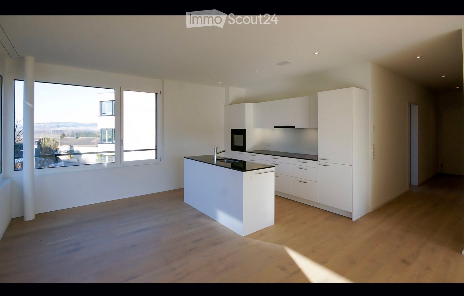 Modern, minimalist kitchen with white cabinets, a central island, and large windows offering a view of the outdoor area.