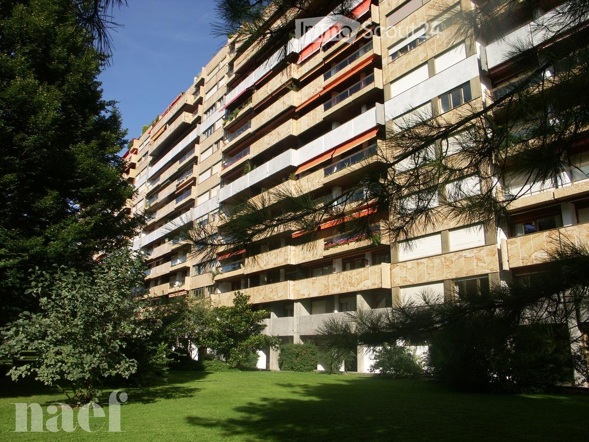 A multi-story residential building with balconies and greenery in the foreground.