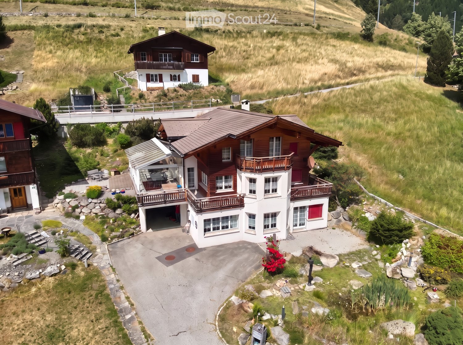Aerial view of a two-story house with a garage, balconies, and a well-maintained garden in a rural setting.